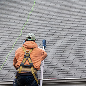 Worker with an orange jacket on a ladder about to climb onto the roof to inspect it