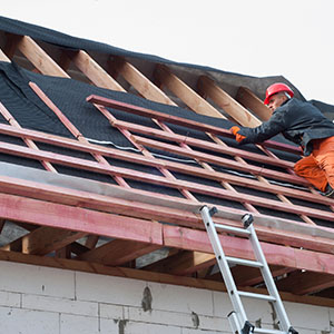 Worker with red helmet installing a new roof by starting with adding in the wooden beams underneath