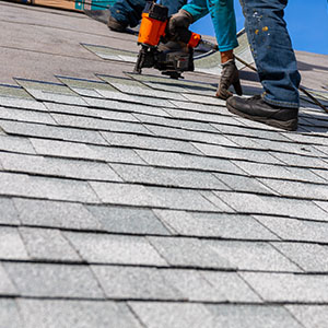 Worker using a nail gun to install new gray shingles on a roof