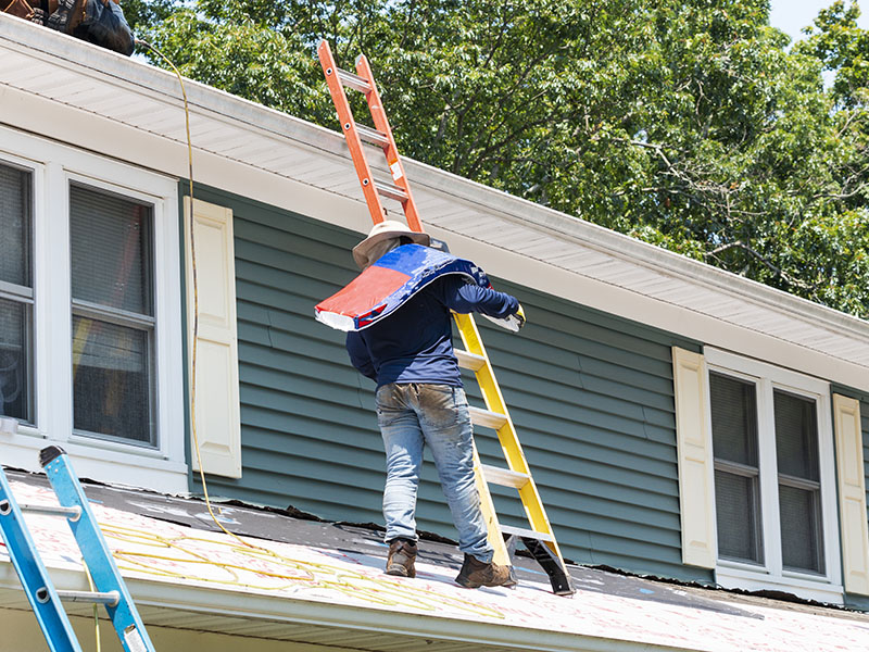 Worker on a residential roof holding a package of shingles over his shoulder in order to replace the roof